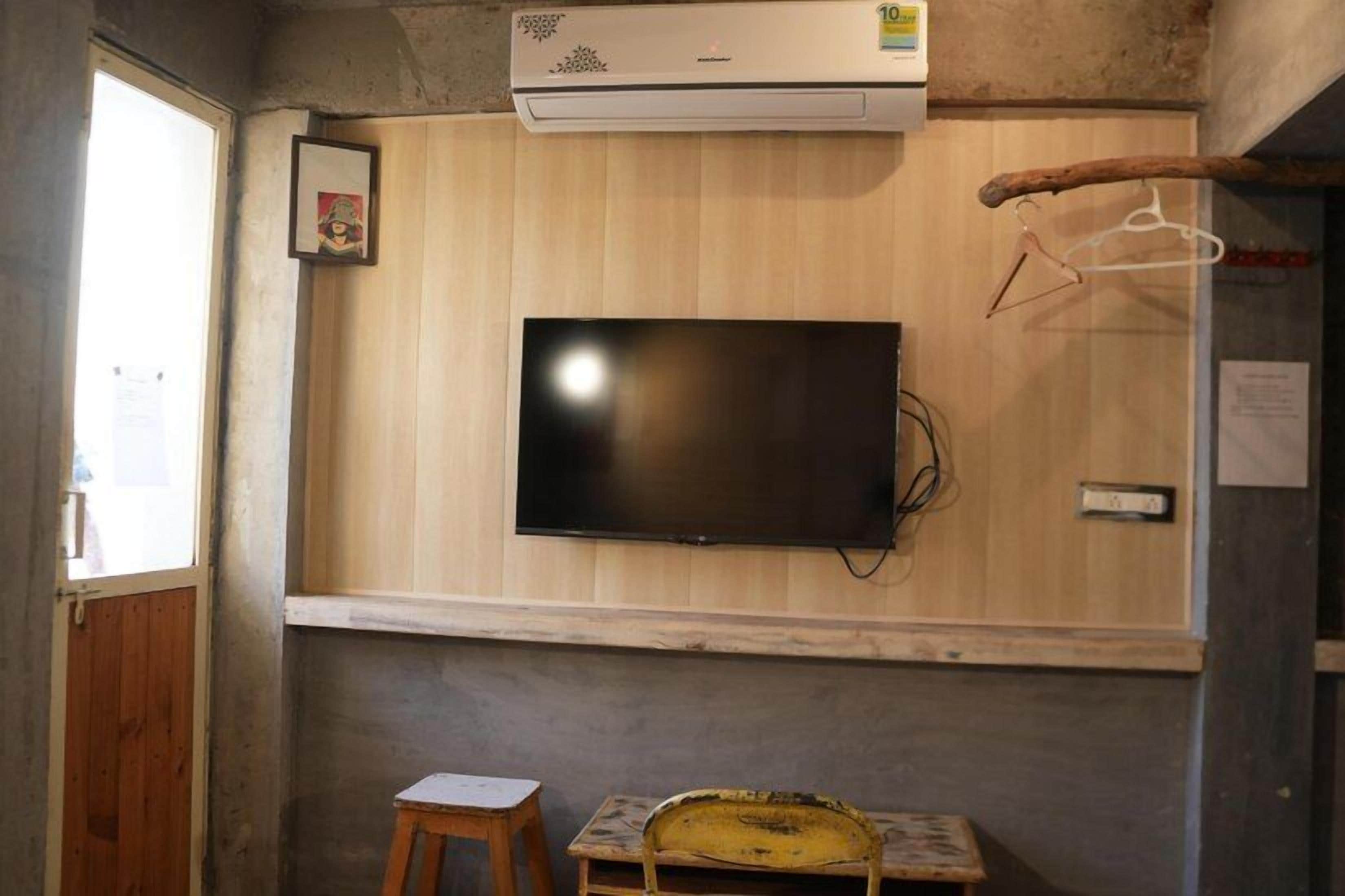 Une pièce équipée d’un téléviseur fixé au mur, d’un petit tabouret et d’un climatiseur mural.