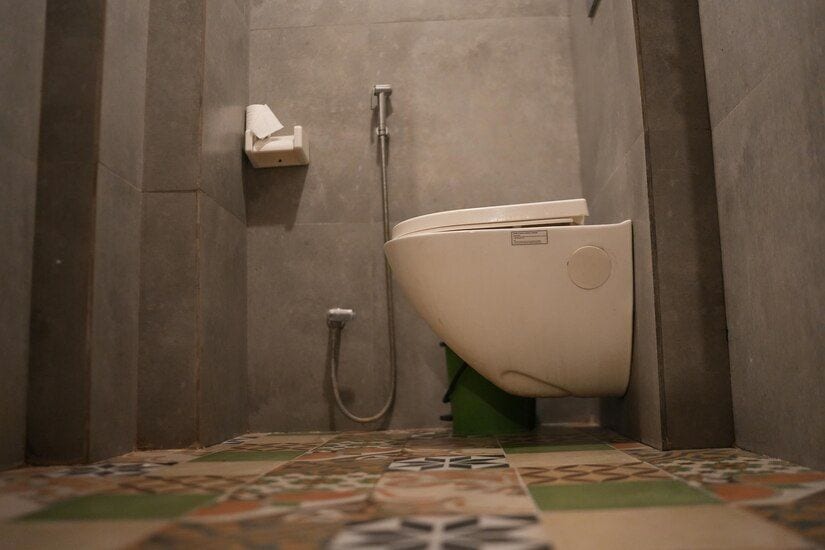 A bathroom with a toilet, a paper towel dispenser, and a shower head.