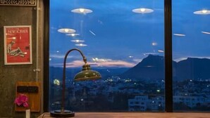 Una habitación con un gran ventanal, una mesa con sillas y lámparas colgantes.