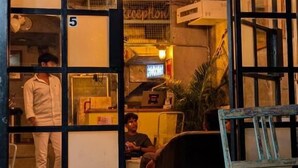 Entrada de un hotel con mostrador de recepción, un letrero con el número 5 y un perro dormido afuera.