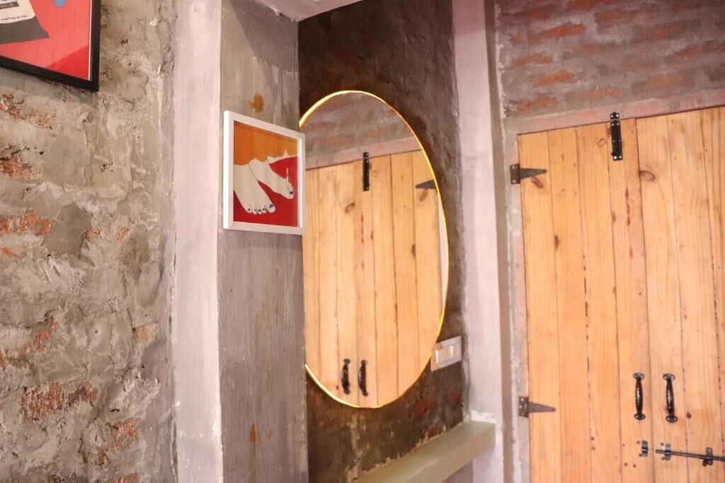 A rustic bathroom with a wooden door, a round mirror, and a hand washing sign.