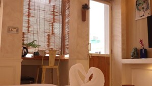 Una habitación con cama, escritorio, silla, ventana con persianas y estante con adornos.