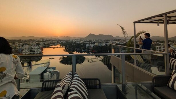 Un balcón con vista a un paisaje urbano y montañas al atardecer.