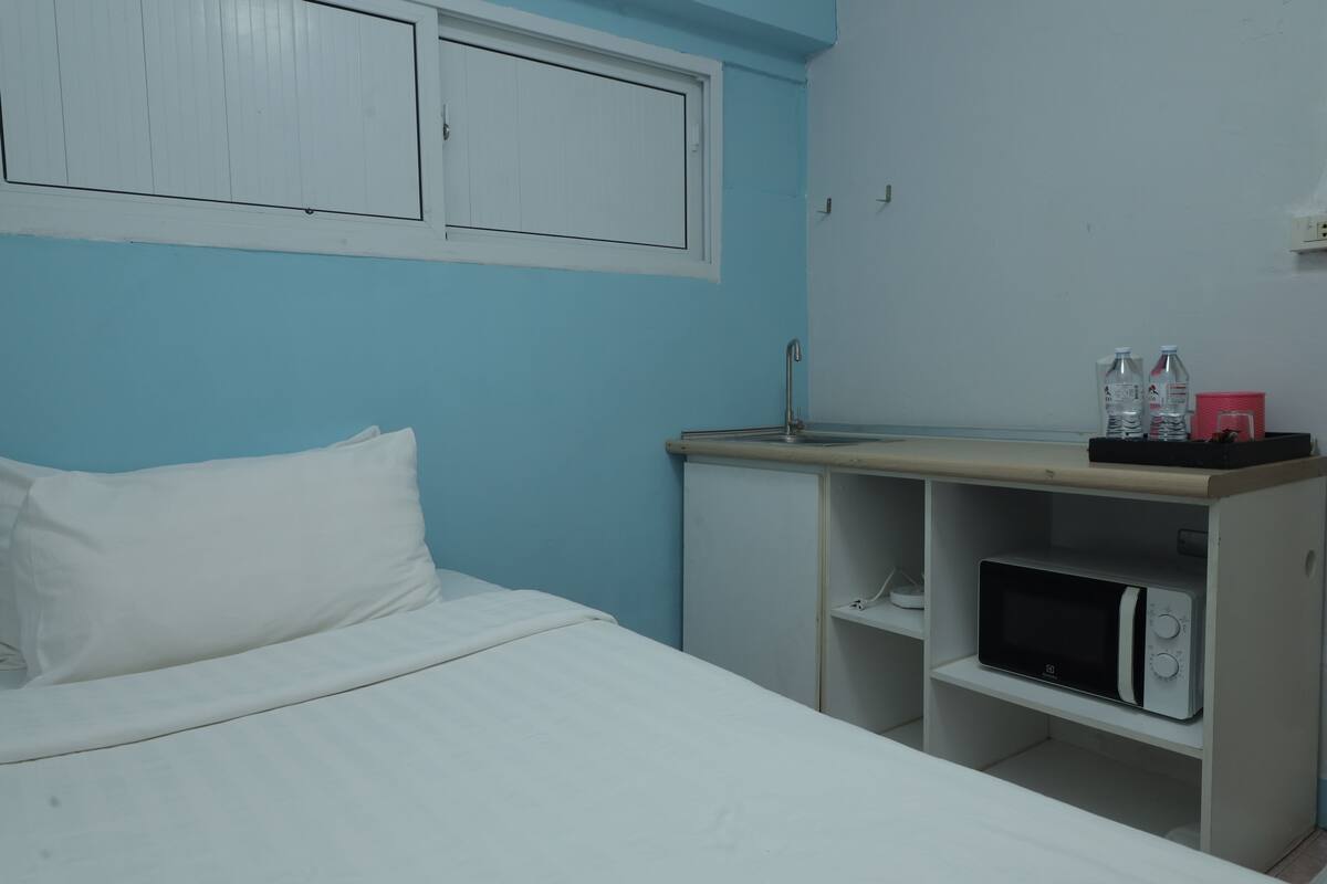 A bedroom with a bed, a wardrobe, a microwave, and a shelf with bottles.