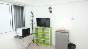 A compact living space with a kitchenette, a flat-screen TV, a green shelving unit, and a small refrigerator. - Happy Residences Pattaya 2 (Pattaya)