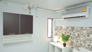 A room with a white air conditioner, a window with a view, a plant on a bedside table, and a wall-mounted cabinet. - Happy Residences Pattaya 2 (Pattaya)