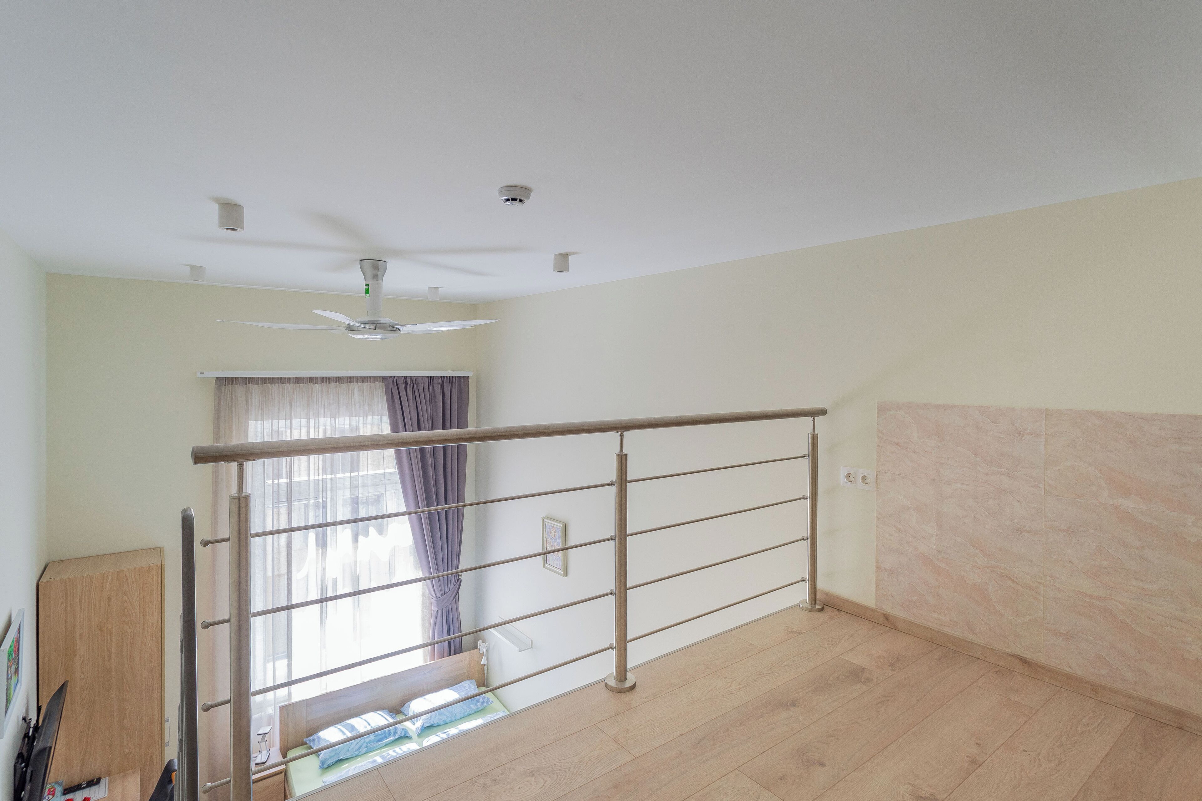 A room with a bed, a window with curtains, a ceiling fan, and a wooden floor.