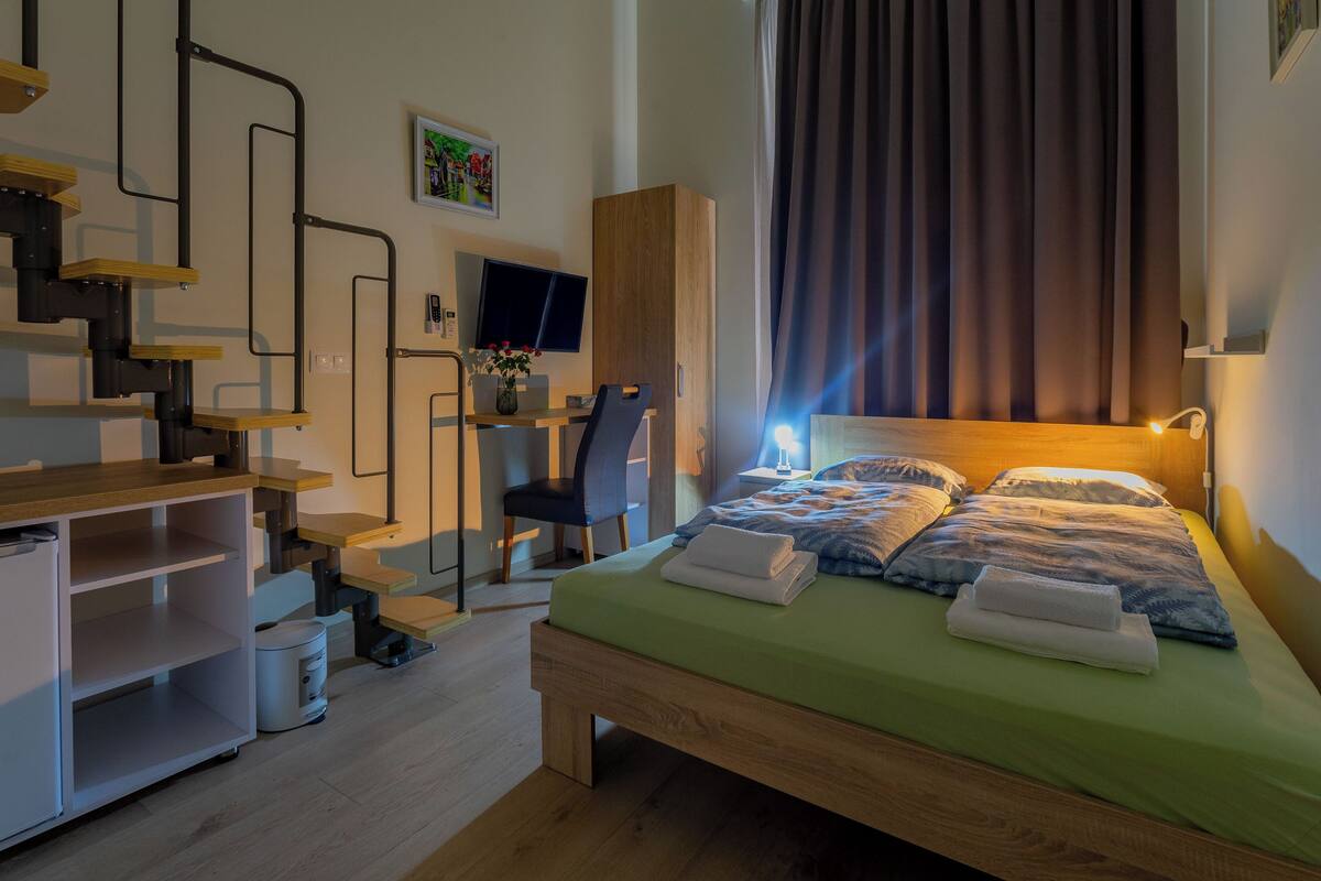 A bedroom with a bed, a desk, a chair, a staircase, and a television.