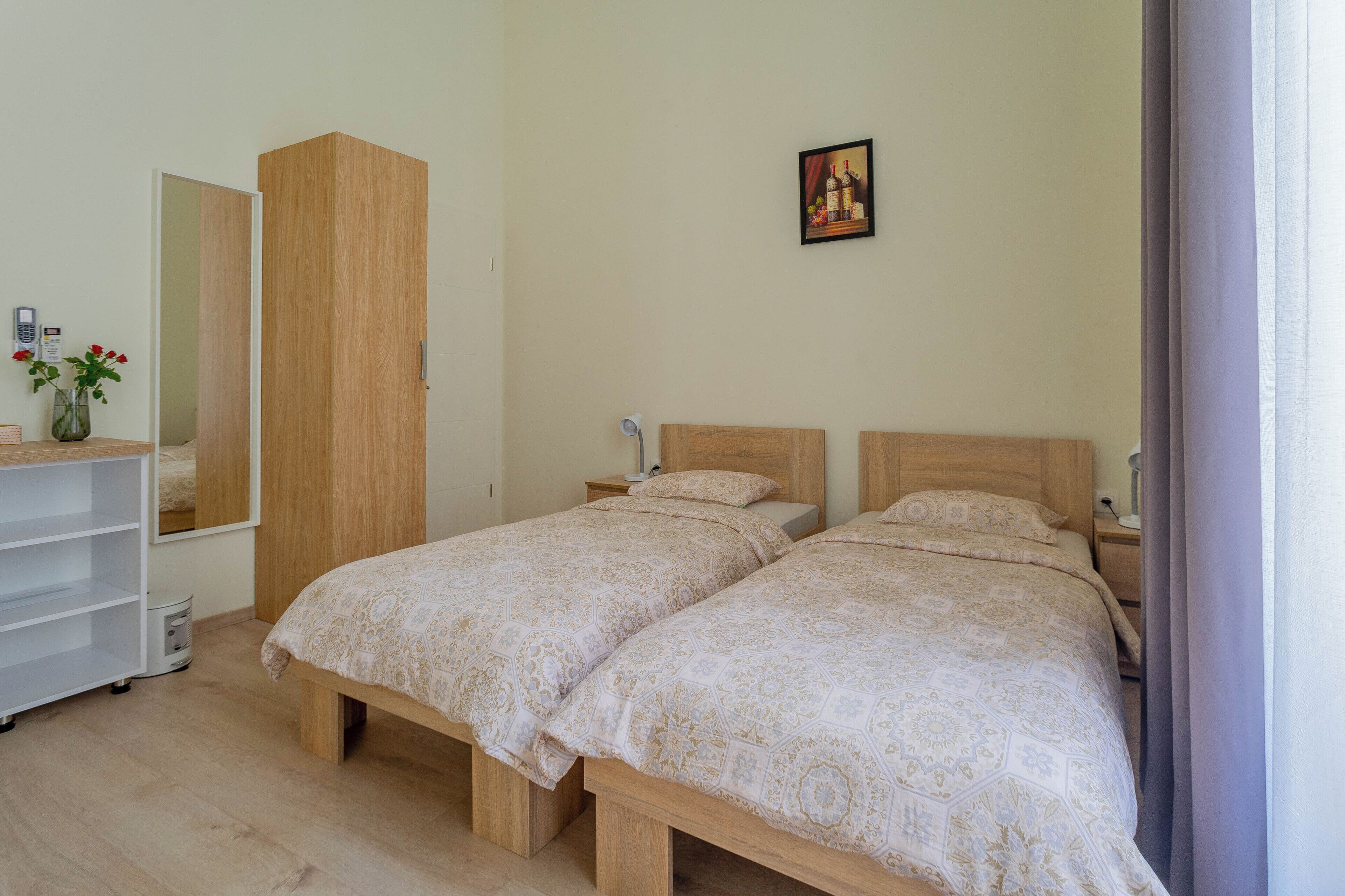 A bedroom with two beds, a wardrobe, a bedside table, a lamp, and a mirror.