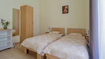 A bedroom with two beds, a wardrobe, a bedside table, a lamp, and a mirror.