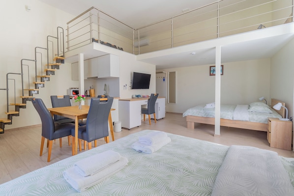 A modern, multi-level room with a dining area, kitchenette, and a bed with a view.