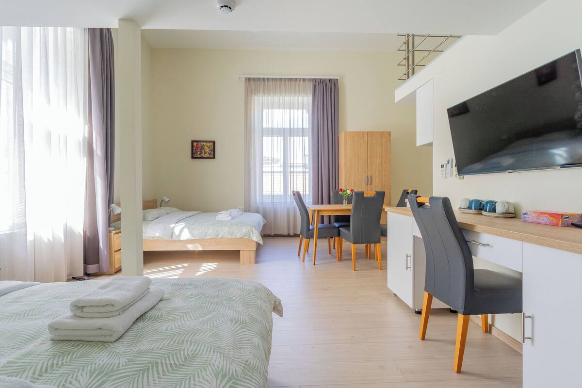 A hotel room with a bed, a desk, a chair, a TV, and a window with curtains.