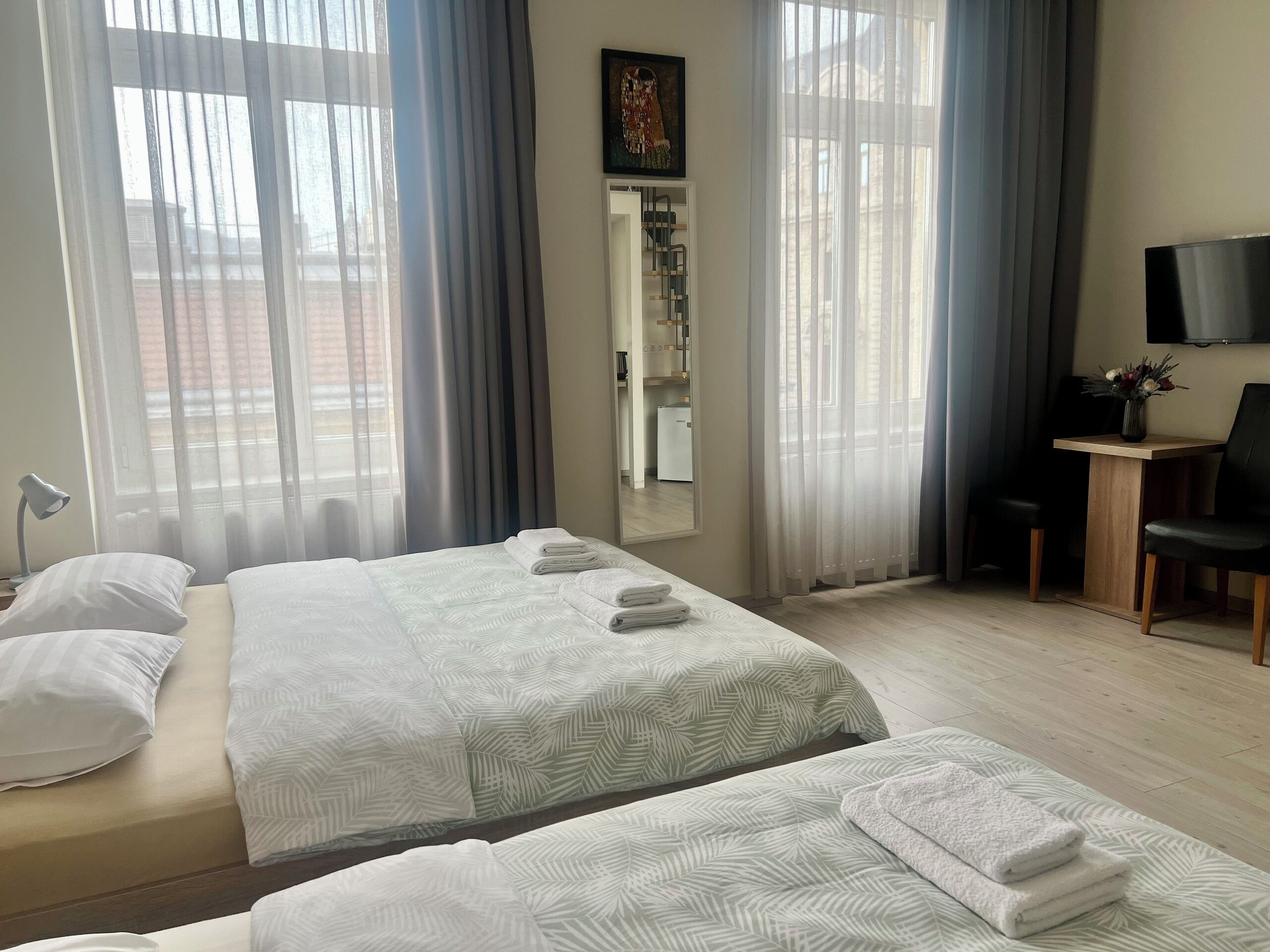A hotel room with two beds, a desk, a chair, a TV, and a bathroom visible through a door.
