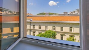 A view through a window of a building with a tiled roof, a tree in front, and a clear sky.