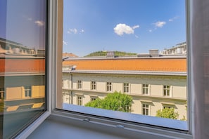 A view through a window of a building with a tiled roof, a tree in front, and a clear sky.