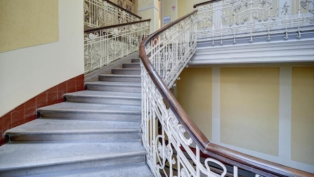 A staircase with ornate white railings and a wooden handrail, leading to an upper floor.