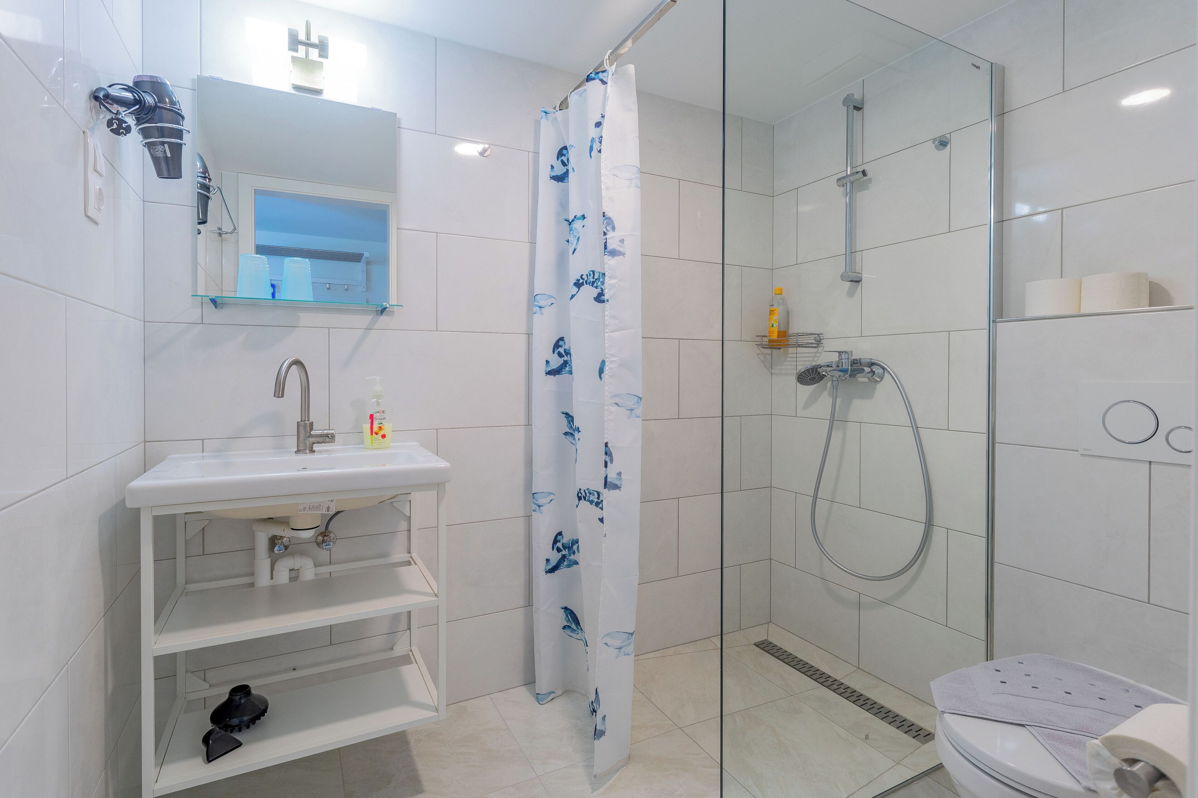 A bathroom with a glass shower enclosure, a white sink with a mirror above it, and a toilet with a towel on it.