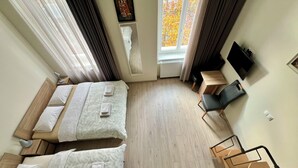 A hotel room with two beds, a desk, a chair, a TV, and a window with autumn leaves.