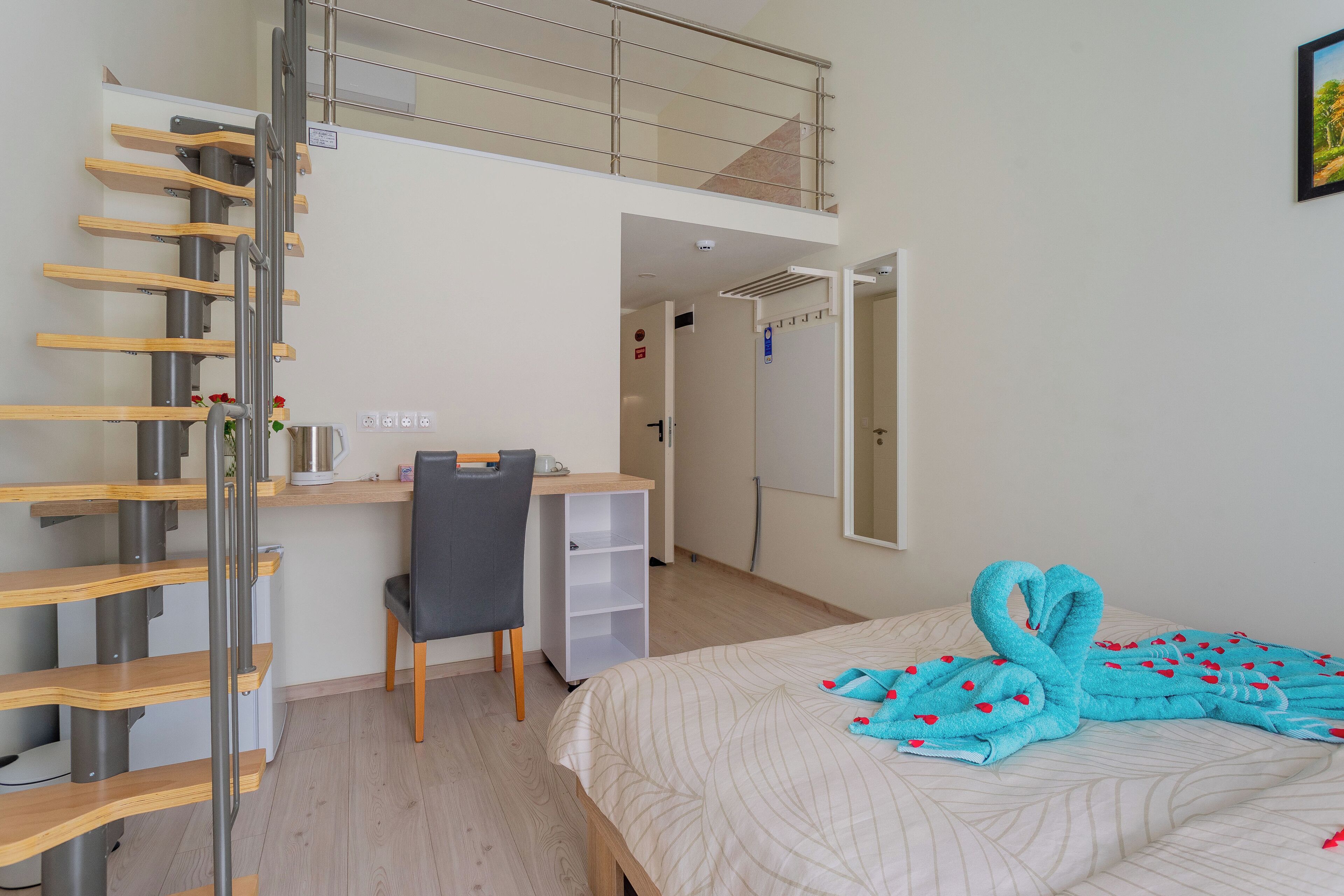 A hotel room with a bed, a desk, a chair, a staircase, and a door leading to another room.