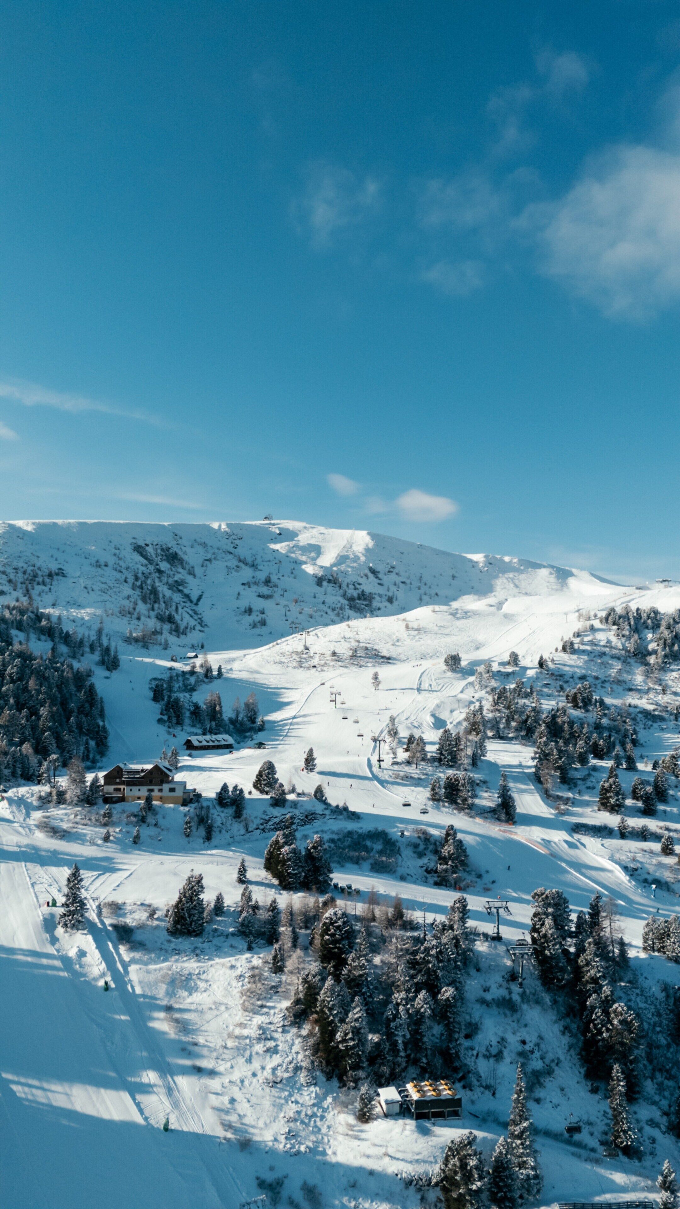 A snow-covered mountain landscape with ski slopes, a lodge, and a clear blue sky.