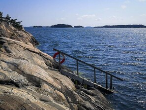 A rocky shoreline with a metal railing and a red lifebuoy. - 5 Star Holiday Home in Navekvarn (Navekvarn)
