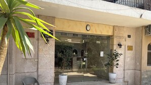 A building entrance with a stone facade, a large potted plant, a bench, and a clear glass door. - Casa de Lama ~ Expat friendly, 2 Bedrooms, A/C (Degla Maadi)