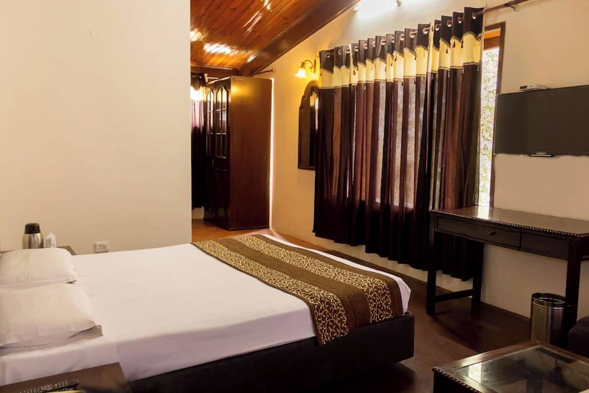 Una habitación de hotel con cama, escritorio, espejo y cortinas.