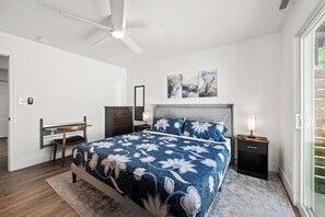 Ein Schlafzimmer mit Bett, Nachttischen, Schreibtisch, Deckenventilator und Bildern an der Wand.