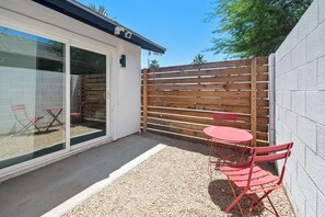 Eine Terrasse mit Tisch und Stühlen, ein Holzzaun und ein weißes Gebäude mit Glastür.