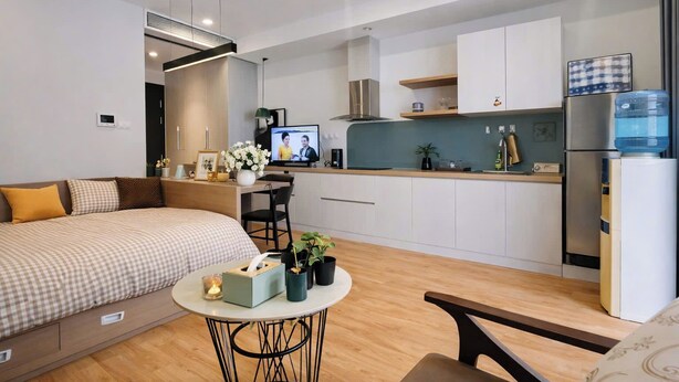 A modern hotel room with a bed, a small dining table, a kitchen area, and a TV. - Vinhomes D'capital Pearl of Hanoi (Hanoi)