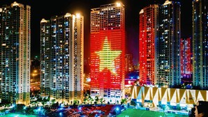 A nighttime view of high-rise buildings with illuminated windows and a prominent building with a red star. - Vinhomes D'capital Pearl of Hanoi (Hanoi)