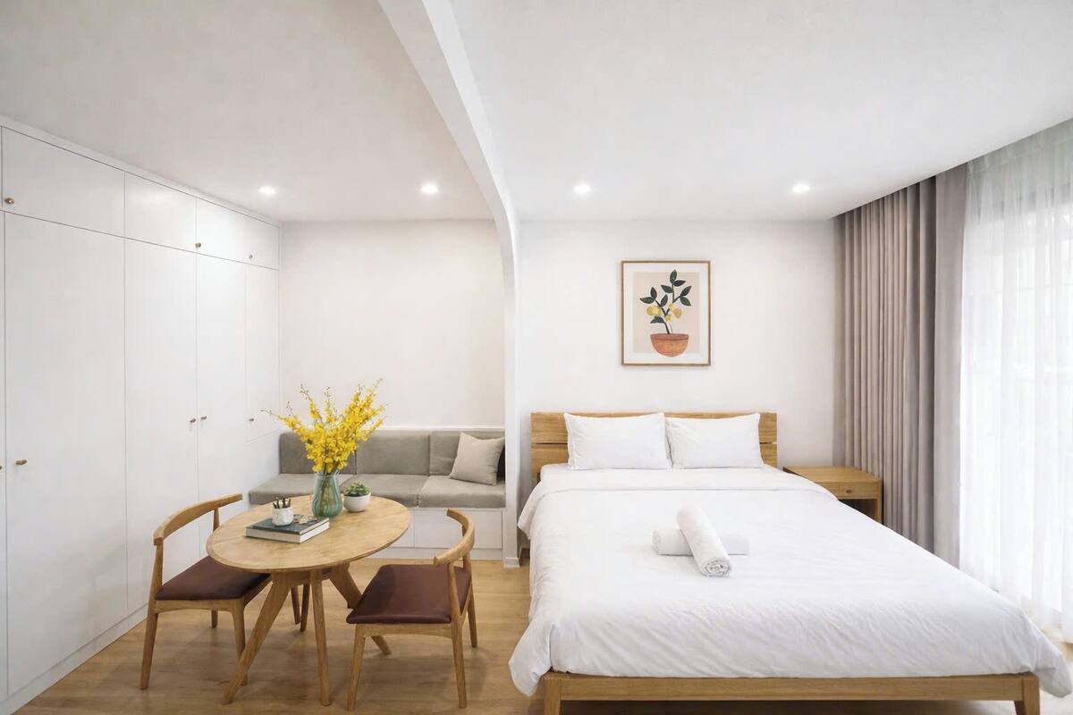 A hotel room with a bed, a sofa, a dining table with chairs, and a potted plant.