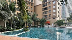 A swimming pool surrounded by a wooden deck, with palm trees and a building in the background. - Vinhomes D'capital Pearl of Hanoi (Hanoi)