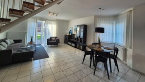 Un salon moderne avec un escalier, un canapé, une table à manger avec des chaises, un téléviseur et une grande fenêtre avec des rideaux.