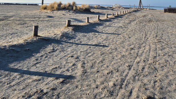 Une plage de sable avec une promenade en bois menant à un poste de surveillance des sauveteurs.