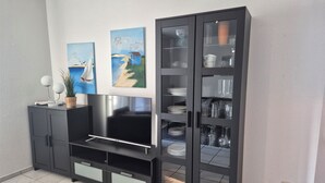 Un salon moderne doté d’un téléviseur à écran plat, d’un meuble avec des portes en verre et de deux tableaux accrochés au mur.
