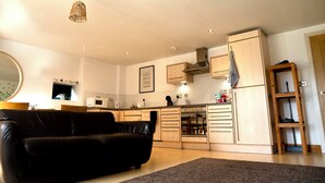 A modern kitchen with wooden cabinets, a black leather sofa, and a dining area. - The Comfort Hub, Leeds Train Station (Leeds)