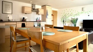 A modern kitchen with wooden cabinetry, a dining table with chairs, and a hanging light fixture. - The Comfort Hub, Leeds Train Station (Leeds)