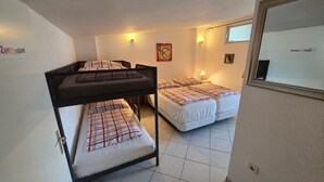 Quarto em dormitório com beliches, duas camas de solteiro, uma janela e luminária fixada na parede.