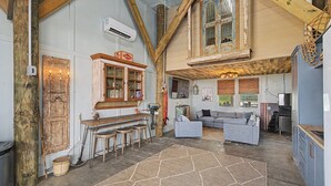 Un interior rústico con vigas de madera a la vista, una zona de bar, un sofá y una cocina.