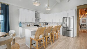 Una cocina moderna con armarios blancos, un refrigerador de acero inoxidable y una isla central con taburetes de bar.
