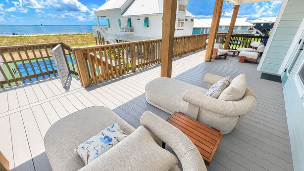 Terraza con mobiliario exterior, baranda de madera y vista a la playa y al océano.