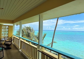 A covered balcony with a view of the ocean, a table with chairs, and a railing.