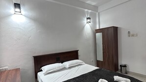 A hotel room with a bed, a wooden wardrobe, a mirror, and a ceiling fan. - Serrena Airport Guest House - Colombo (Seeduwa)