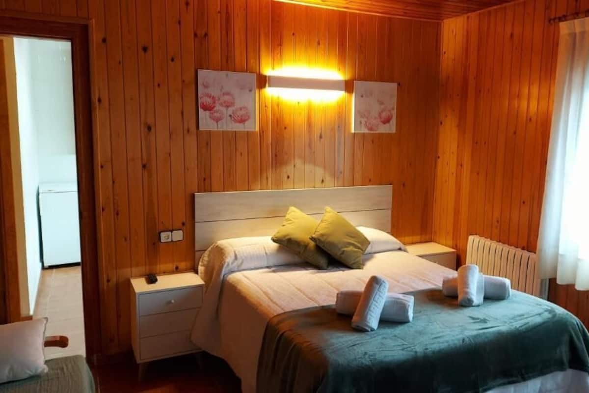 Une pièce aux murs lambrissés, comprenant un lit, des tables de chevet et une fenêtre avec des rideaux.