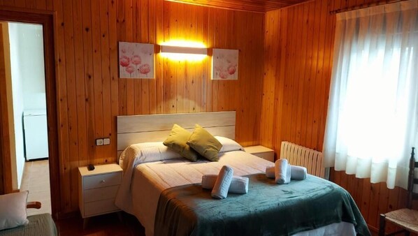 Ein Zimmer mit Holzwänden, einem Bett, Nachttischen und einem Fenster mit Vorhängen.