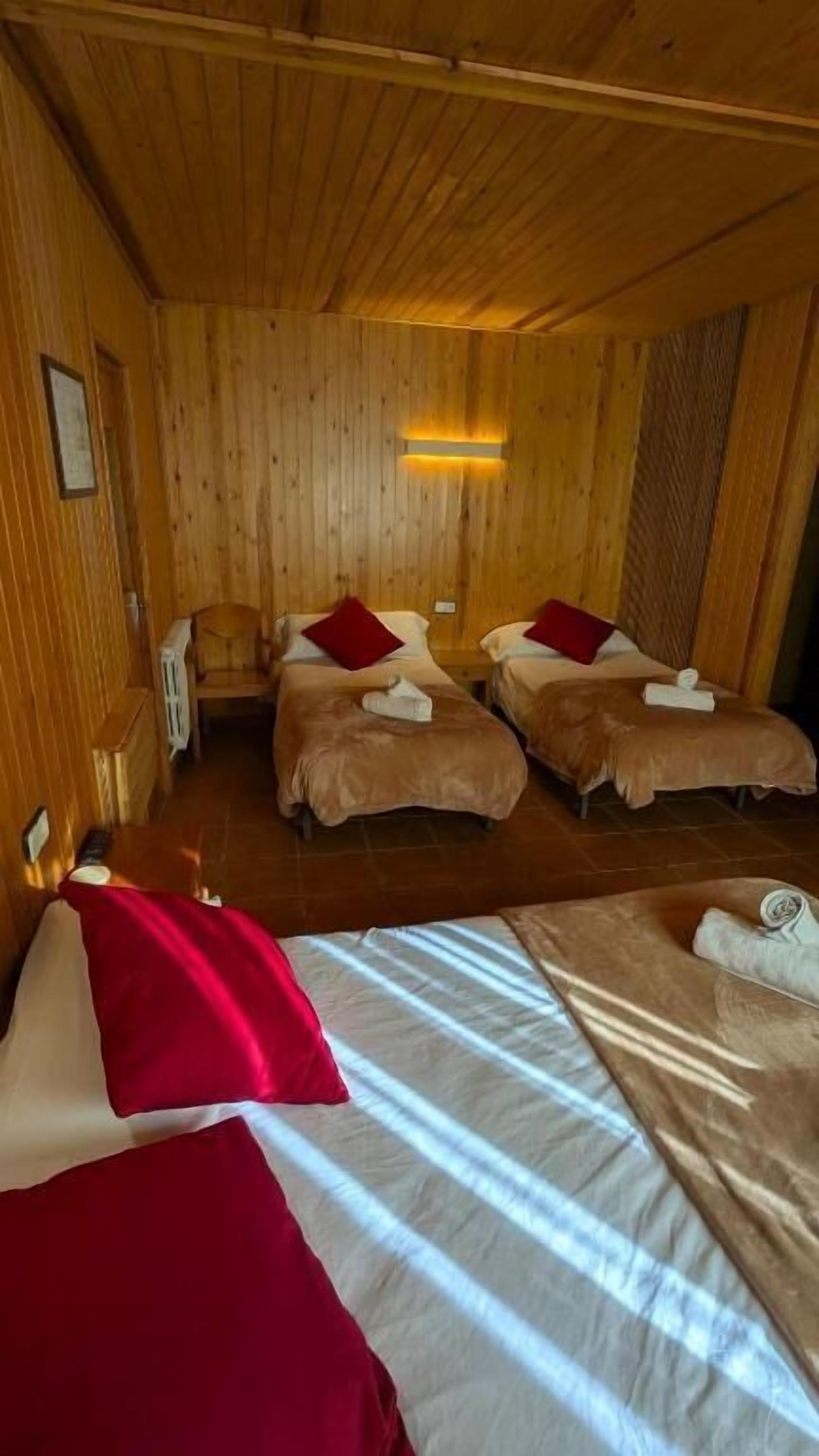 Una habitación de madera con dos camas, cada una con una almohada roja y una colcha blanca.