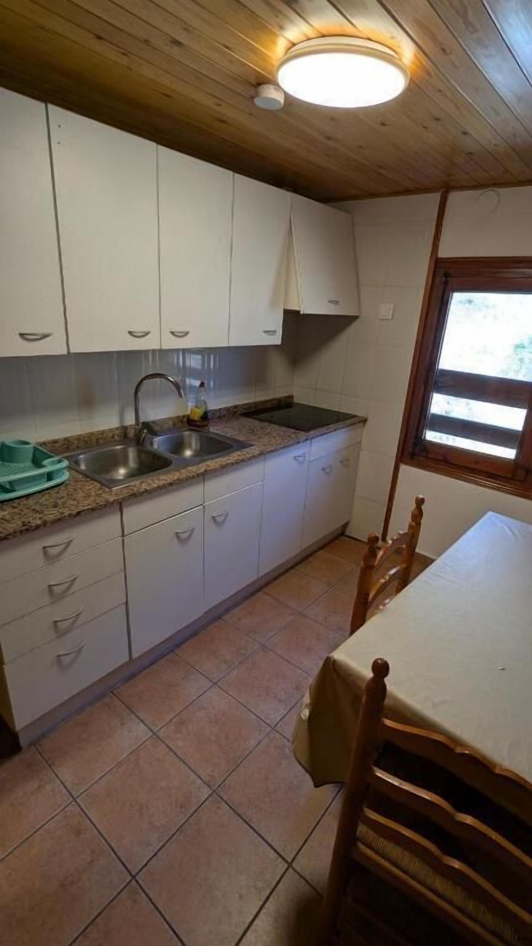 A kitchen with white cabinets, a granite countertop, a sink, and a window with blinds.