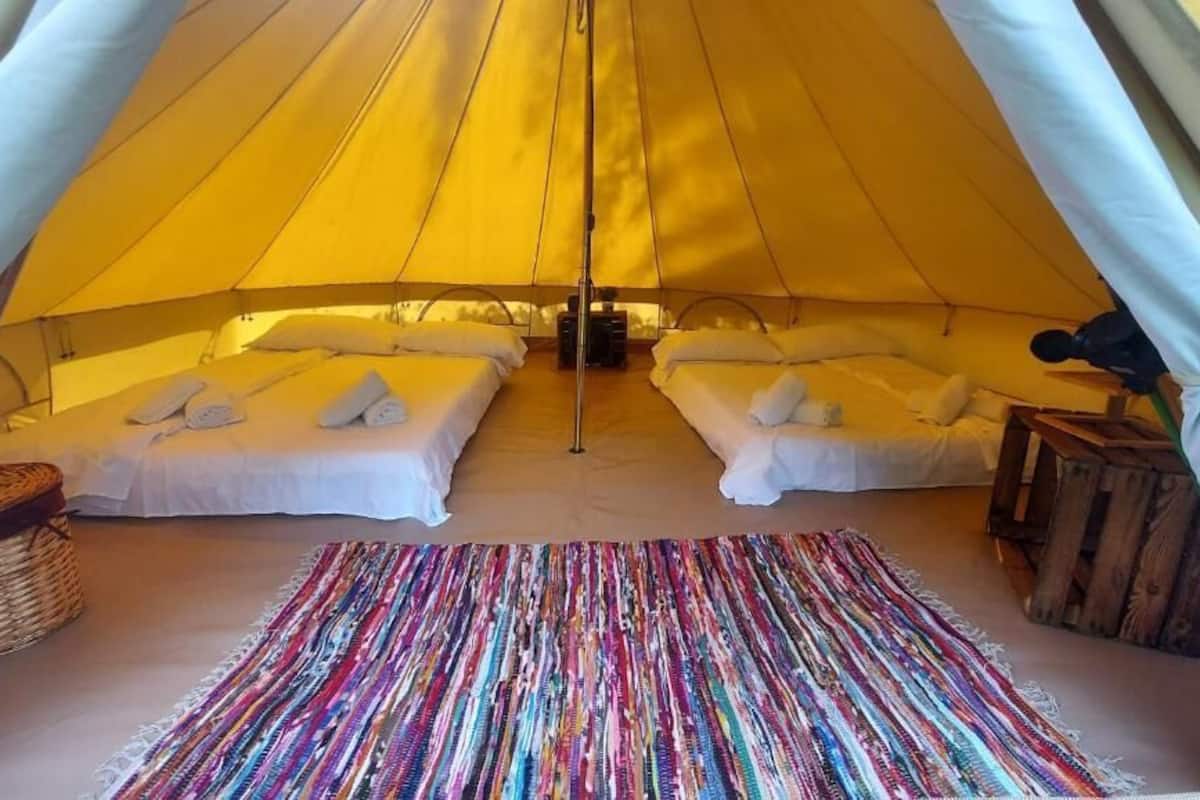 Une tente avec deux lits, un tapis coloré et un tabouret en bois.