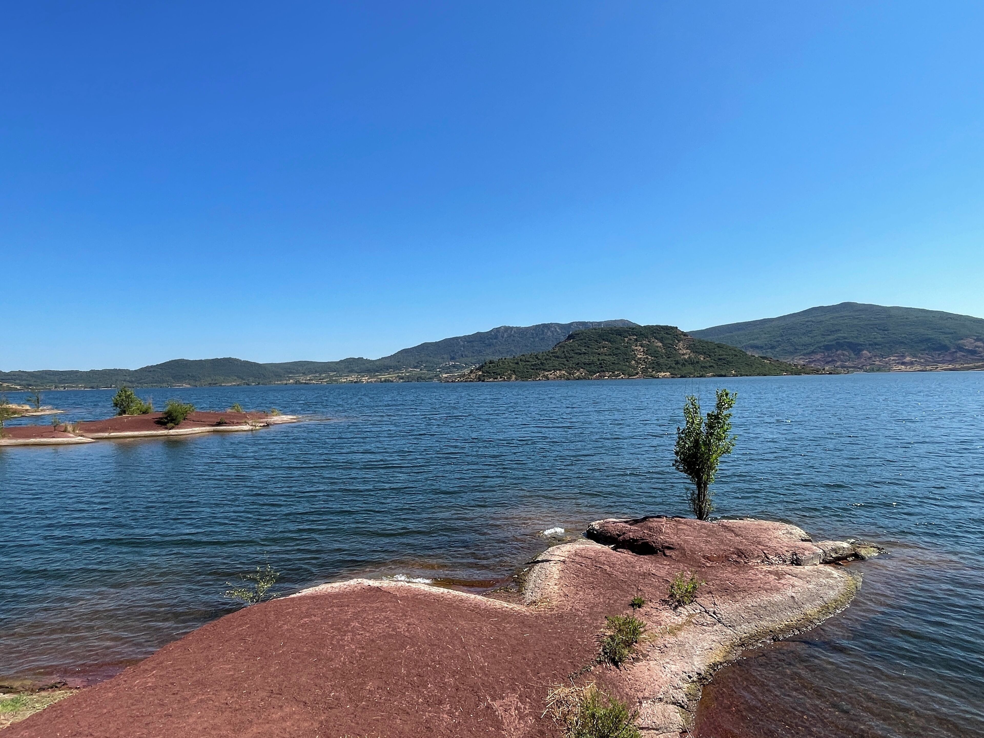 A lake with a rocky shoreline, clear blue sky, and distant mountains.